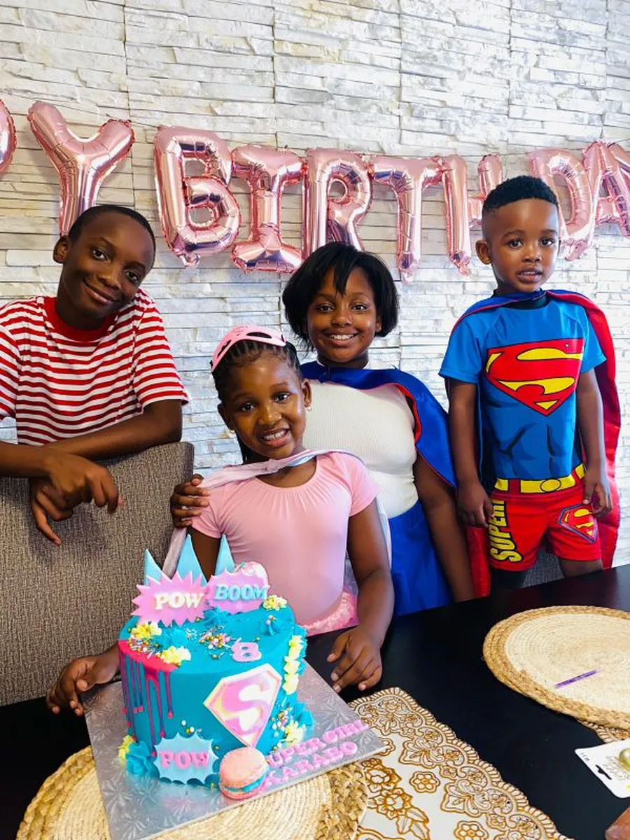 Four children celebrating a birthday party with balloons and a cake