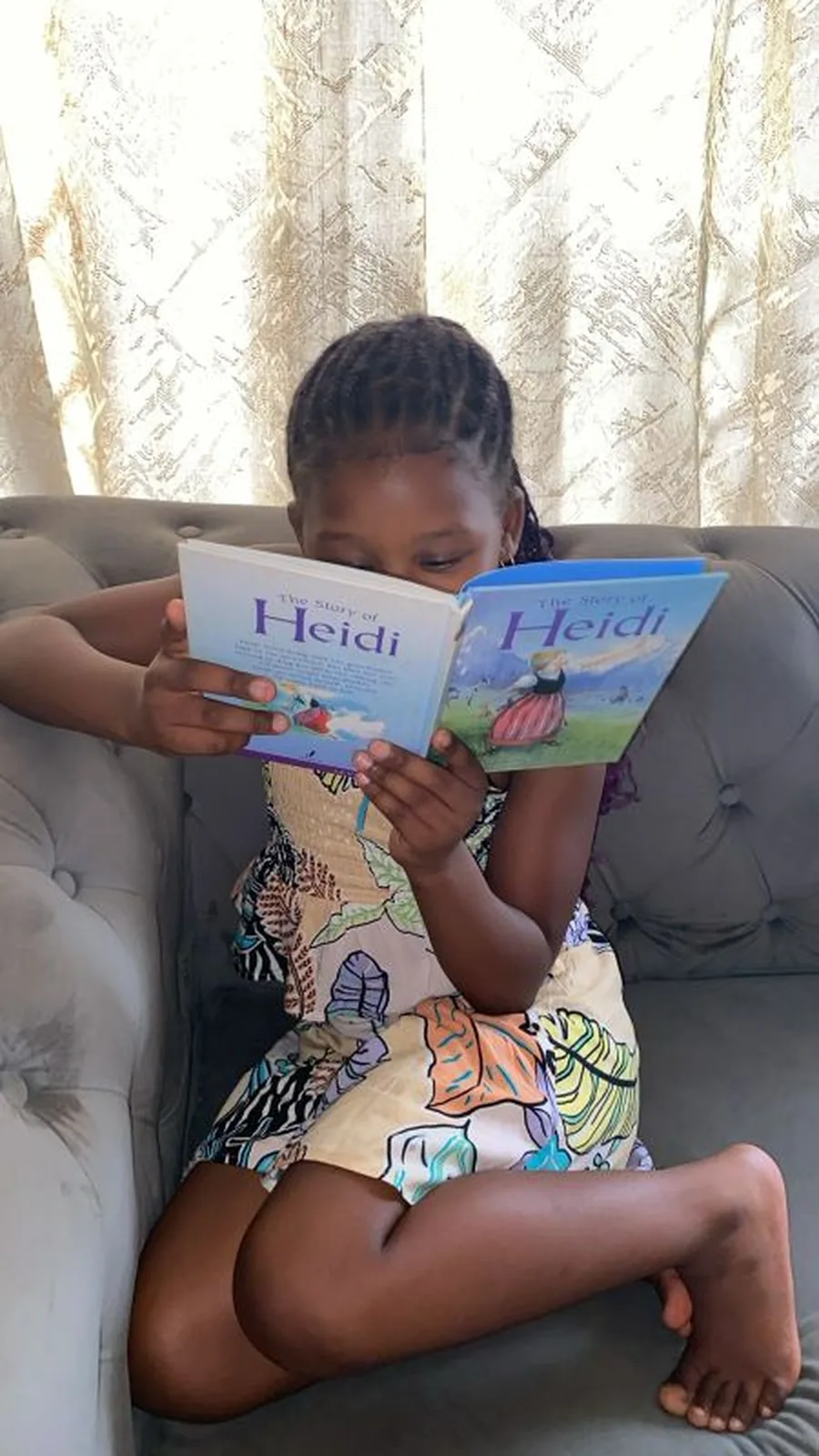 A young girl reading a picture book quietly on the couch